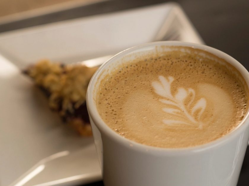Cappuccino mit Latte-Art und ein Stück Gebäck auf einem Teller
